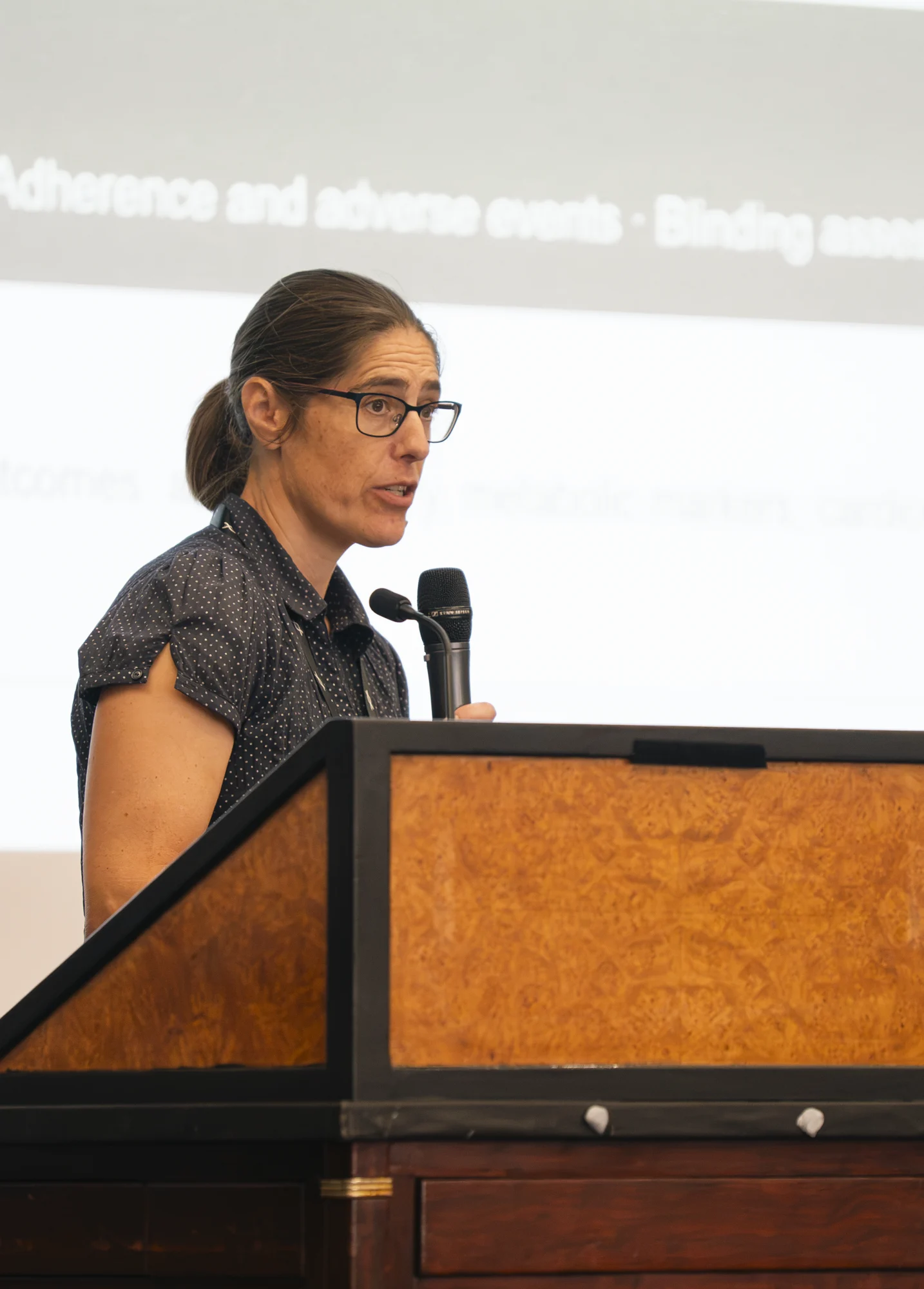 A presenter speaks at the lectern with a research slide projected behind